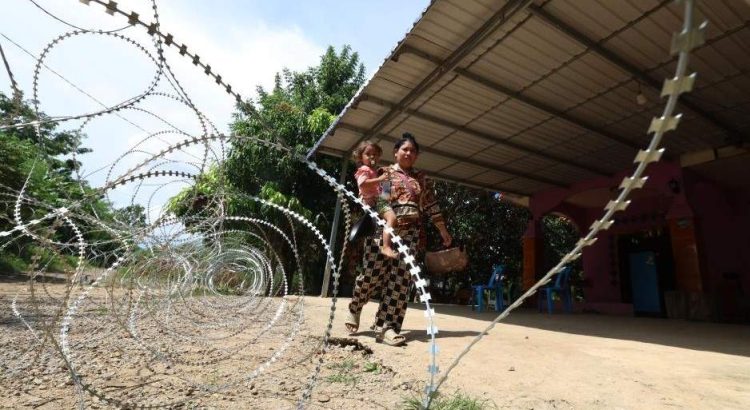 Một phụ nữ bế trẻ đi ngang qua dây thép gai mà Campuchia tố Thái Lan đặt tại tỉnh Banteay Meanchey, ngày 14.8.2025. Ảnh: Xinhua