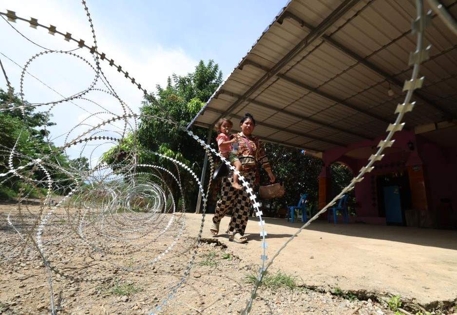 Một phụ nữ bế trẻ đi ngang qua dây thép gai mà Campuchia tố Thái Lan đặt tại tỉnh Banteay Meanchey, ngày 14.8.2025. Ảnh: Xinhua